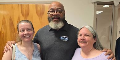 Three people smiling with arms around each other.