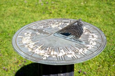 Old metal sundial with owl figure in garden.