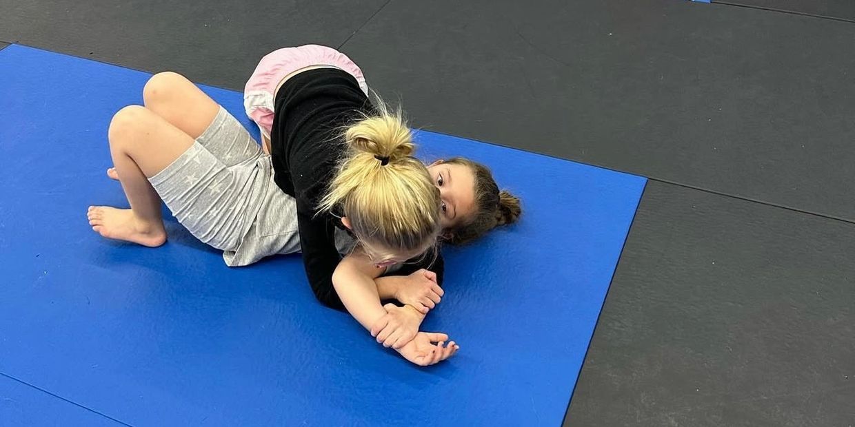 Two kids practicing wrestling on a blue mat.