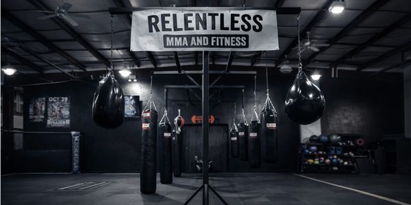 MMA gym with hanging punching bags under a RELENTLESS MMA AND FITNESS banner.