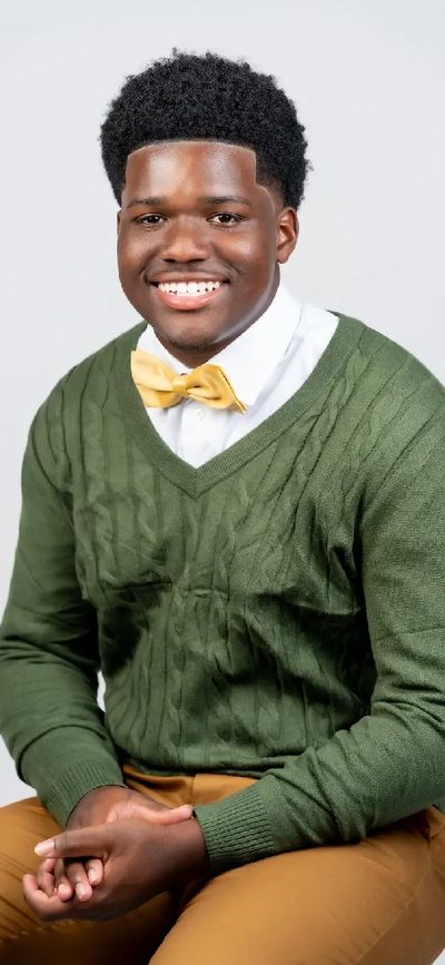 Young man smiling, wearing a green sweater and yellow bow tie.