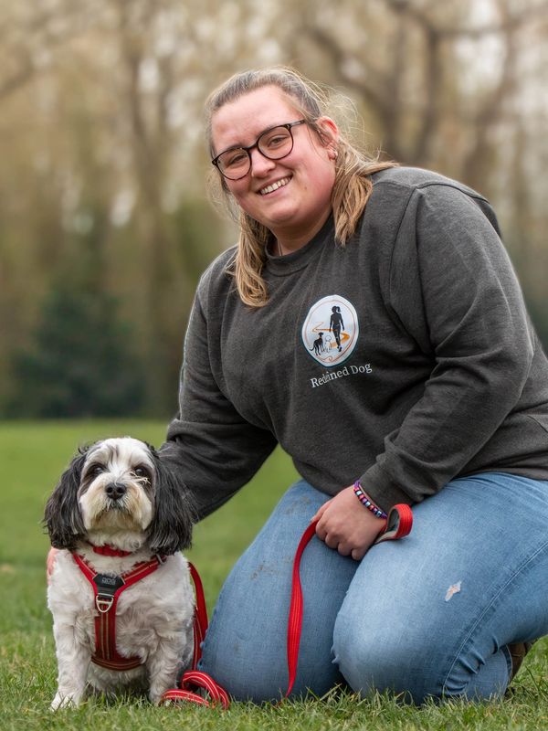 Smiling woman kneels with her small dog in a grassy park.