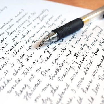 Close-up of a pen resting on handwritten cursive text on white paper.