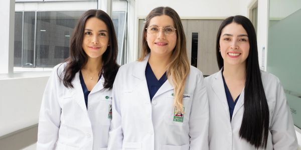 Tres médicas sonrientes con batas blancas en un hospital.