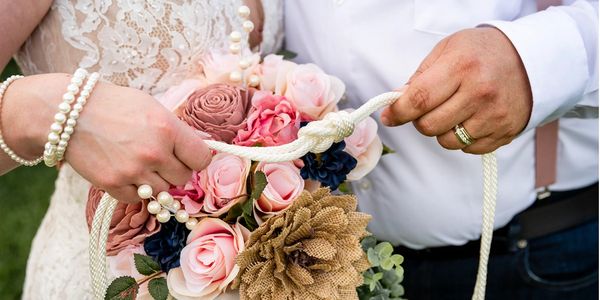 Couple holding a rope and a bouquet of flowers during a wedding ceremony.