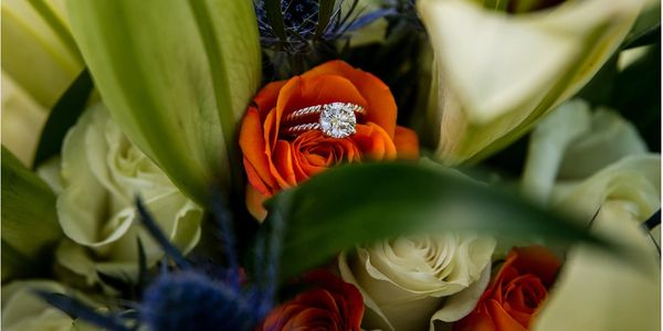 Diamond ring nestled in orange rose among white flowers.