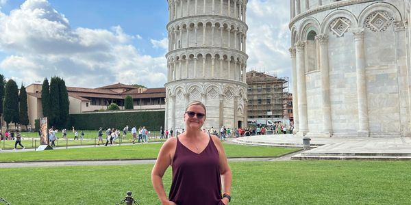 A woman standing in front of the Leaning Tower of Pisa on a sunny day.