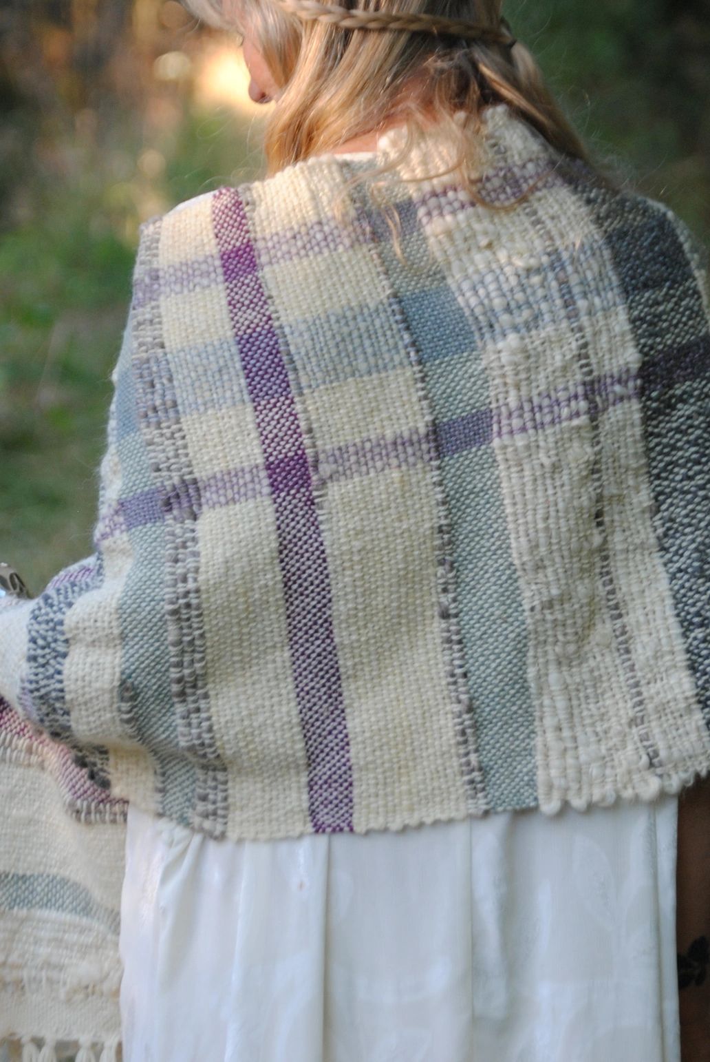 Woman wearing a handwoven plaid shawl outdoors in soft light.