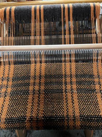 A woven textile on a loom with black and orange threads.