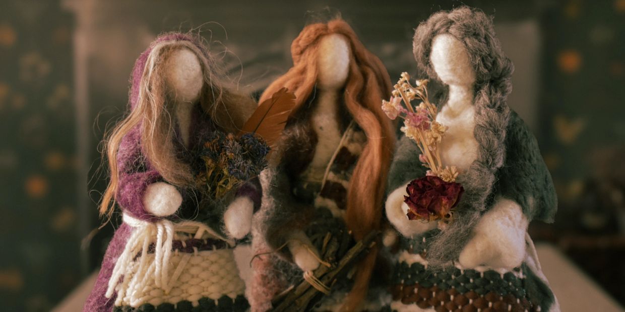 Three handmade woolen dolls holding dried flowers and twigs.