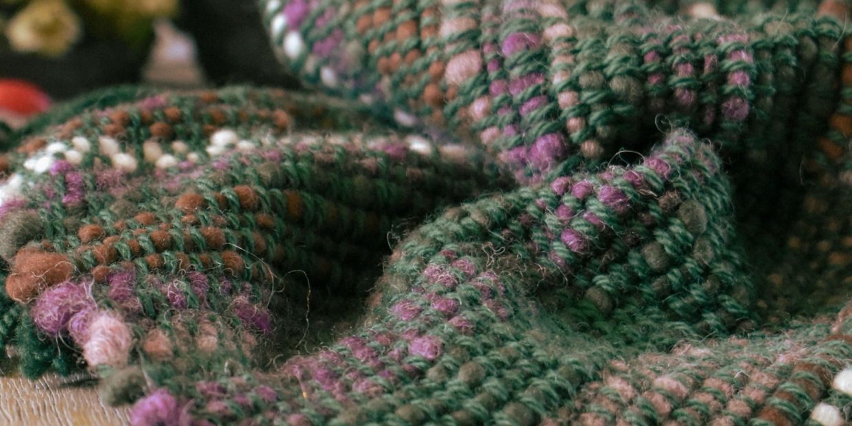 Close-up of colorful knitted fabric with green, purple, and brown yarn.