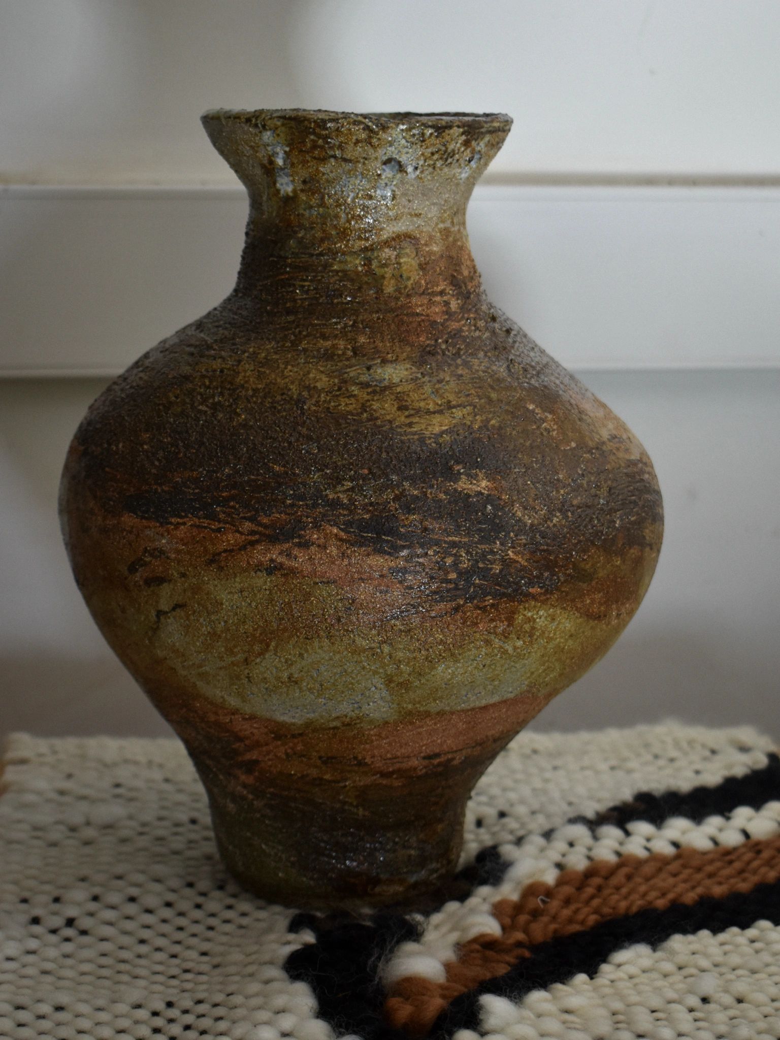 Rustic pottery vase with earthy tones on a textured cloth.
