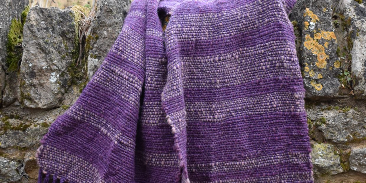 A purple handwoven textile draped over a rustic stone wall.