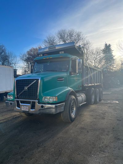 Green Volvo dump truck parked on dirt under a clear sky.