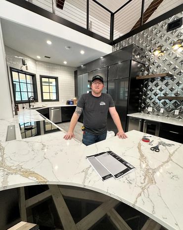 Man standing behind a large marble kitchen countertop in a modern kitchen.