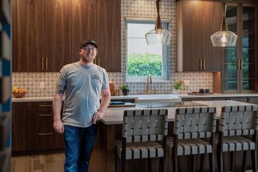 Man standing in a modern kitchen with wooden cabinets and a large island.