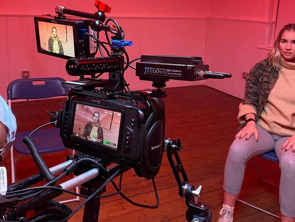 Professional camera setup filming a woman sitting on a chair indoors.