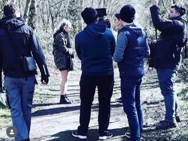 Film crew shoots a woman in a wooded area.