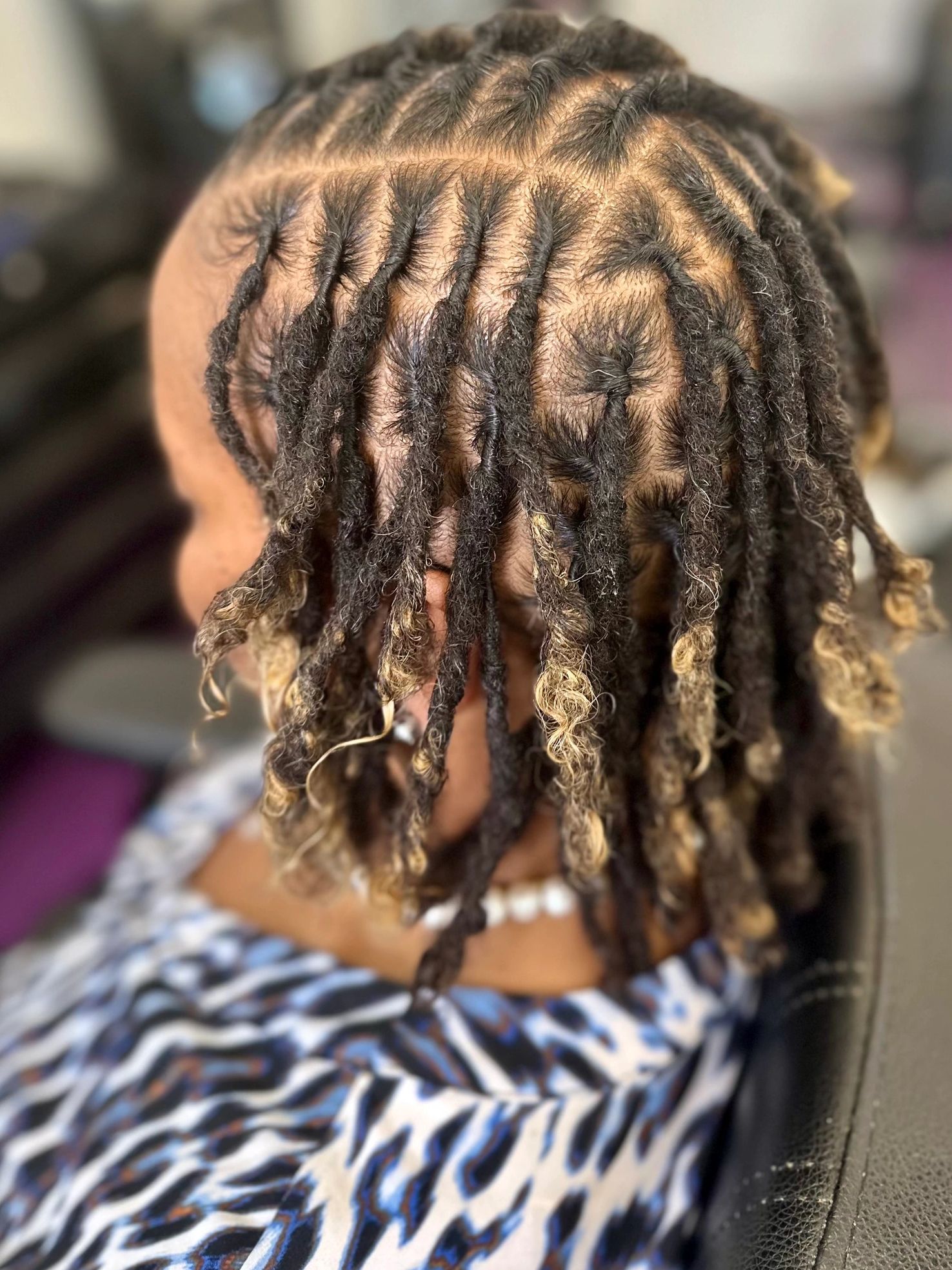 Close-up of neatly twisted dreadlocks with blonde tips on a person wearing a patterned shirt.