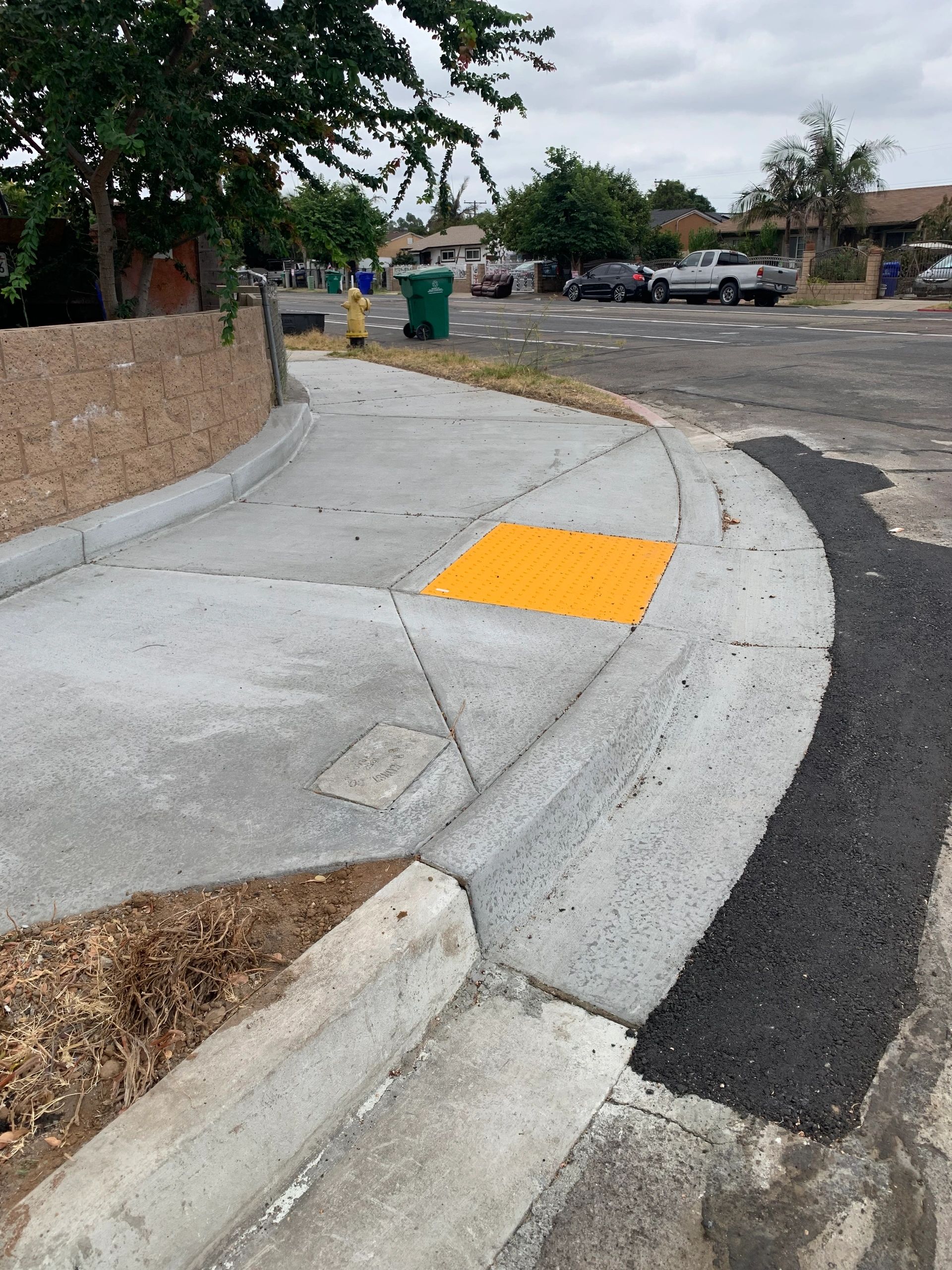 Concrete sidewalk with curb ramp and tactile paving on a residential street corner.