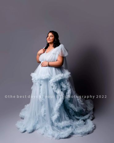Beautiful pregnant woman dressed in sky blue elegant gown while posing with hand on stomach.