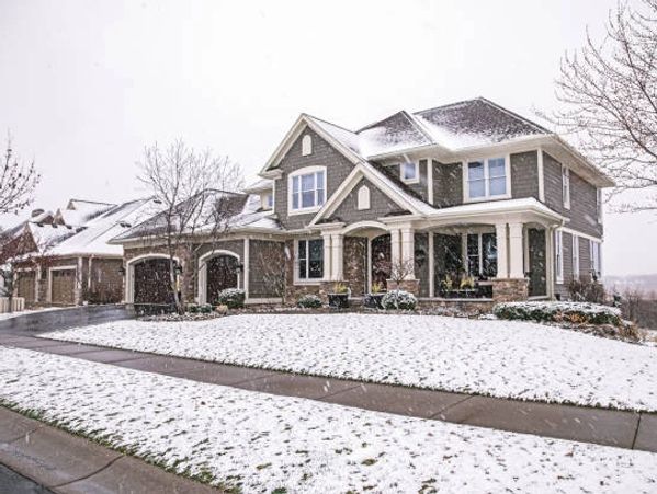 A large gray house with white trim in a light snow-covered suburban neighborhood.