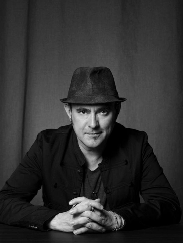 Man in a hat with hands clasped, looking confidently at the camera.