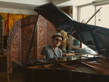 Man in hat and sunglasses playing grand piano in a cozy room.