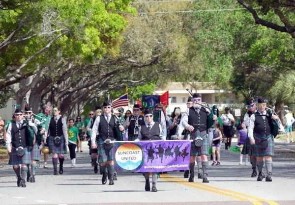 Group of people in kilts playing bagpipes in a parade.
