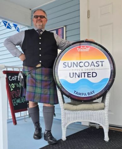 Man in traditional Scottish attire standing next to a drum.