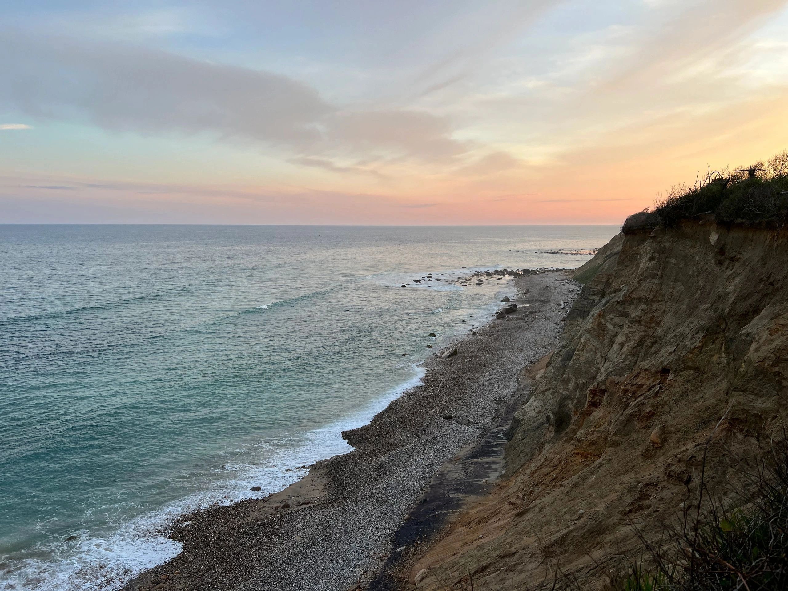 Ocean view at sunset with rocky shoreline.