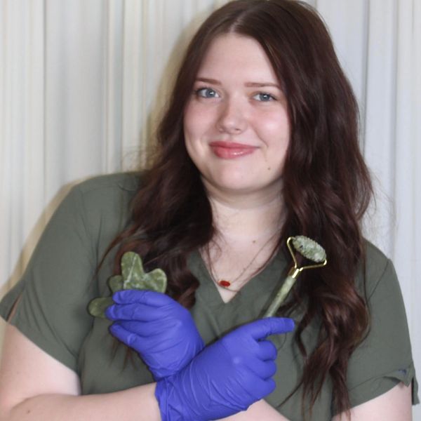 Woman with brown hair wearing blue gloves holding facial massage tools.