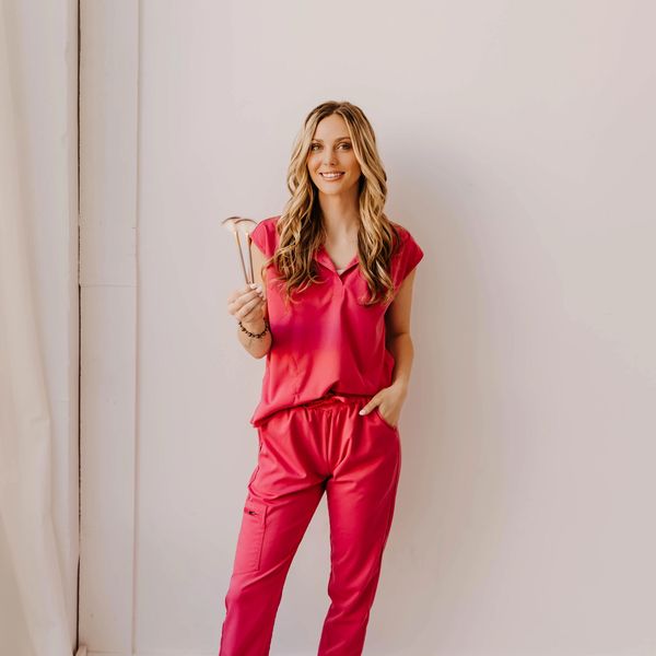 Smiling woman in red scrubs holding medical tools against a plain background.