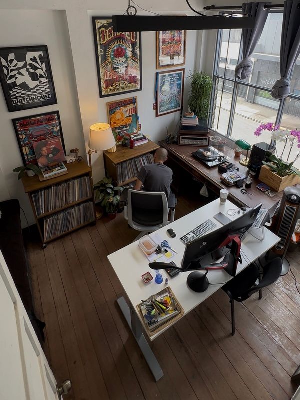 Man sitting in a cozy, art-filled workspace with vinyl records and a computer.