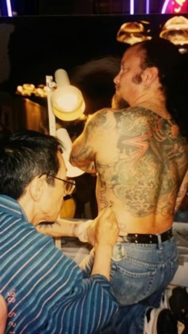 A man is getting a detailed tattoo on his back from an artist.