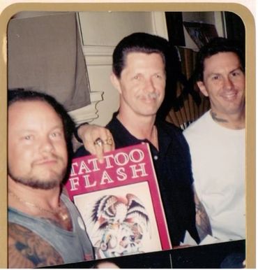 Three men posing with a vintage tattoo flash book.