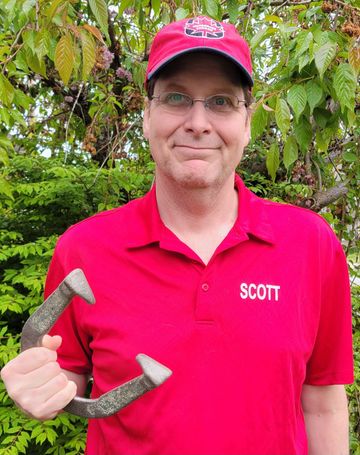 Man in red hat and shirt standing outdoors with greenery.