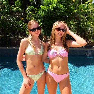 Two young women posing by a pool in bikinis and sunglasses.