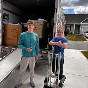 Two young men standing in front of a moving truck with boxes.