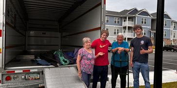 Four people standing by an open moving truck in a residential area.