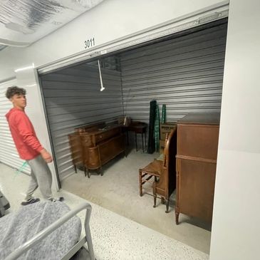 A young man stands near a storage unit filled with wooden furniture.