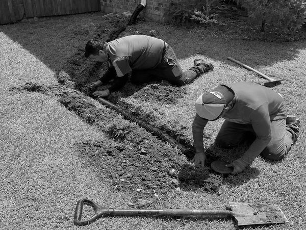 Dos personas trabajando en la instalación de una tubería en el jardín.