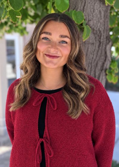 Smiling woman standing outdoors with tree in the background.