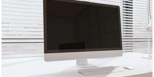 Modern computer setup on a clean white desk with blinds in the background.