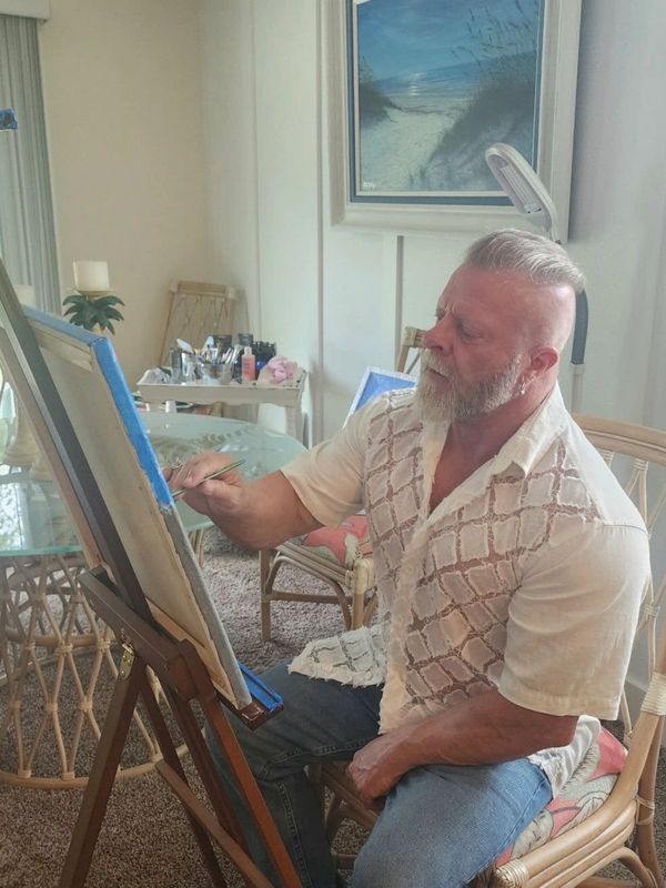 Man with a beard painting on a canvas indoors.