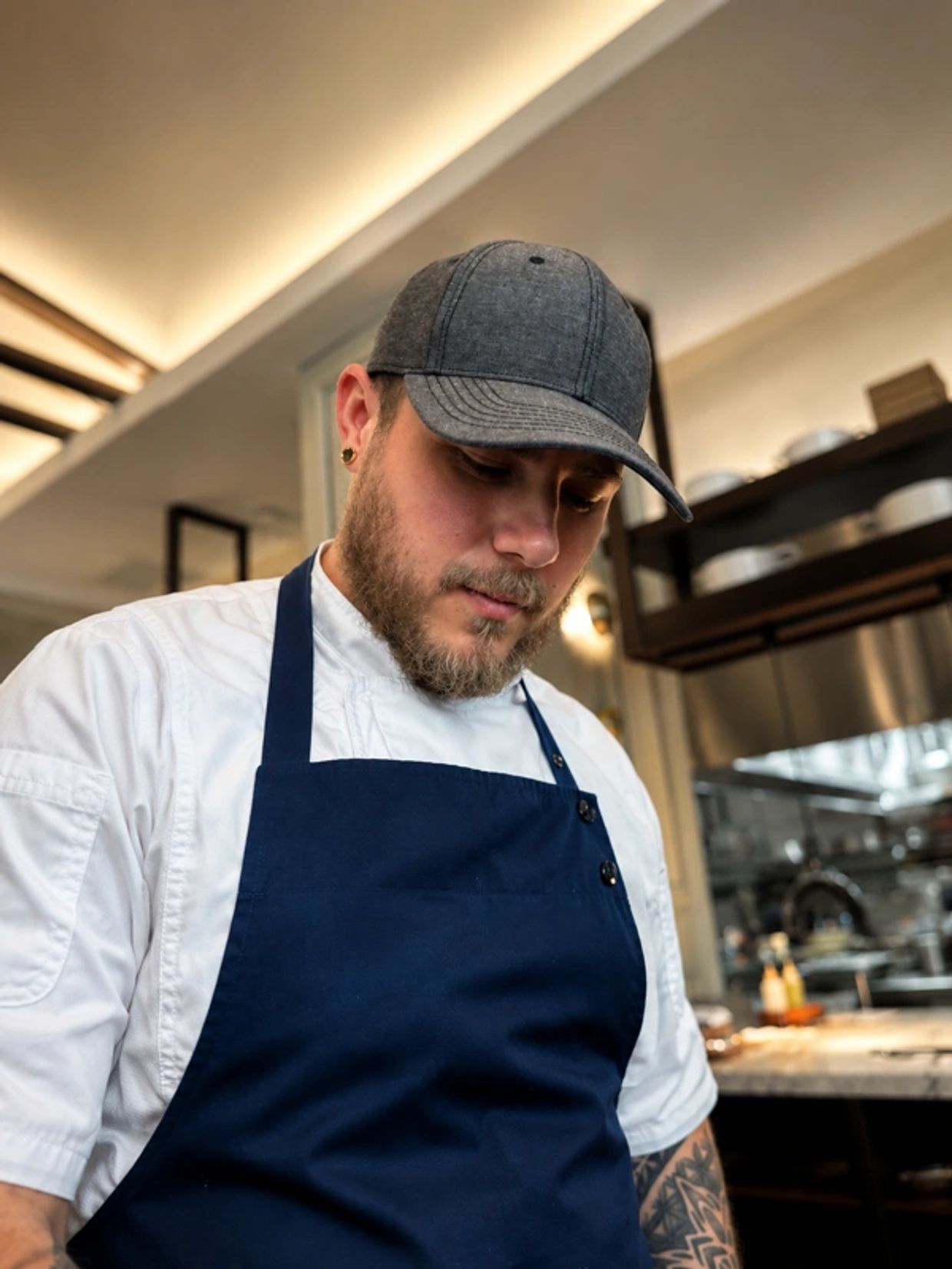 Focused chef wearing a cap and apron in a modern kitchen.