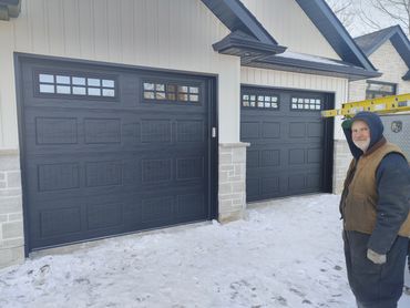 Worker standing next to two black garage doors in snowy weather.