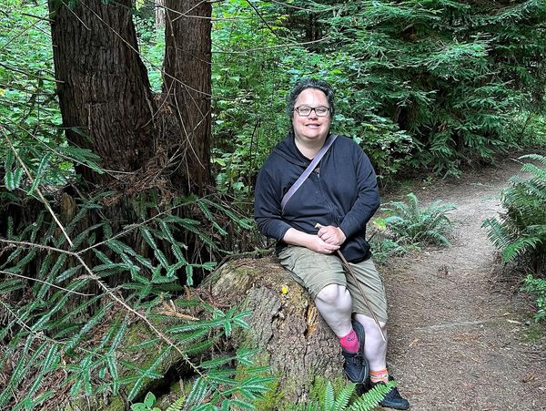 Photo of Holly sitting in the forest near a hiking trail