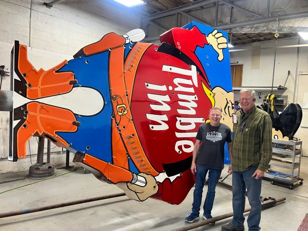 Two men standing next to a giant Popeye sign.