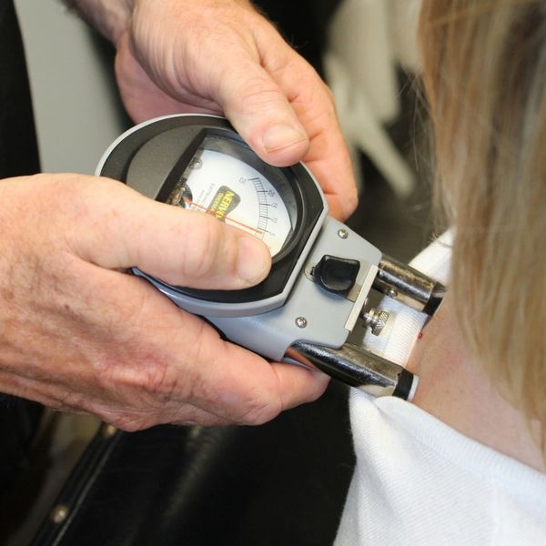 Person measuring body fat with a caliper on the neck.